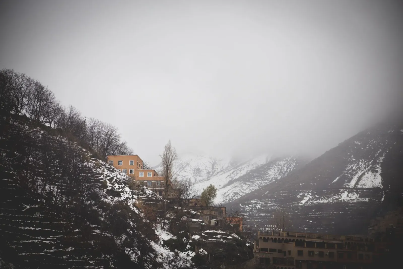 Terraced mountain village dusted with snow beneath low clouds in the High Atlas