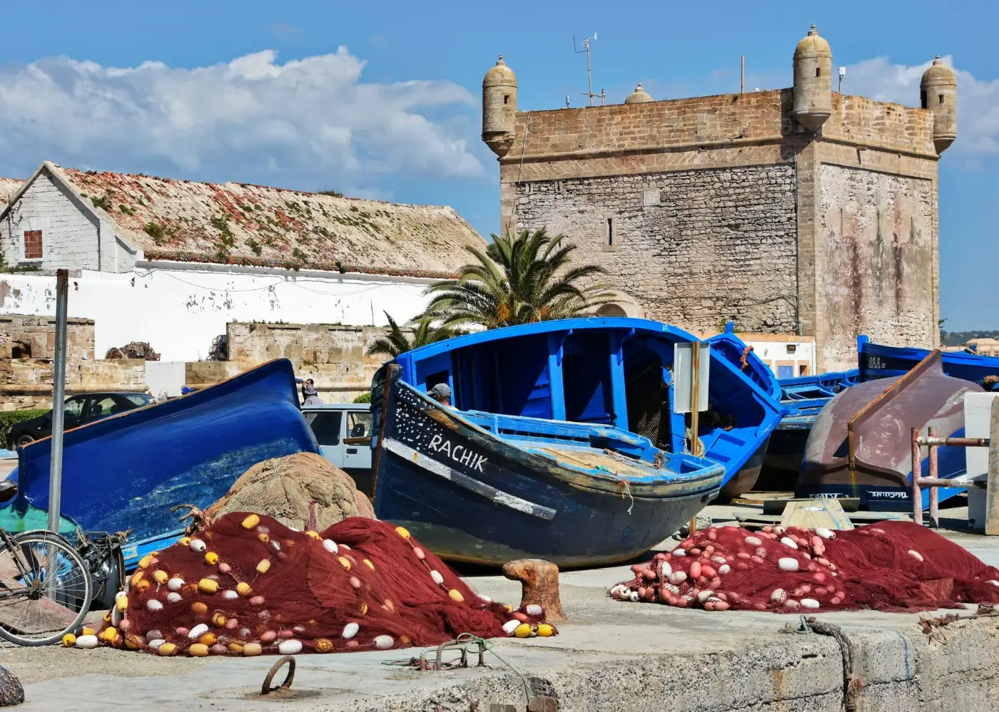 Blue wooden fishing boats and red nets beside the stone sea fortress in Essaouira harbour
