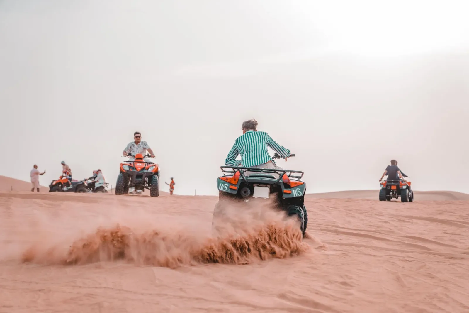 Riders on quad bikes kicking up sand across desert dunes