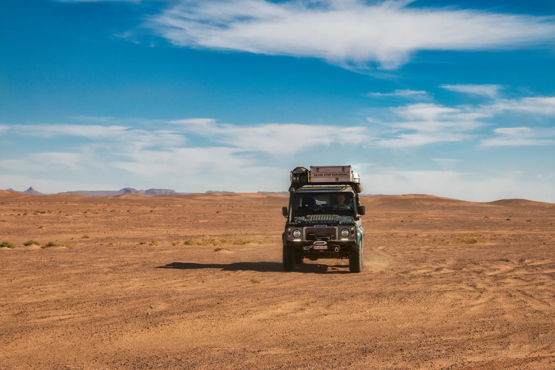 Four-wheel-drive vehicle crossing a wide desert plain under a blue sky