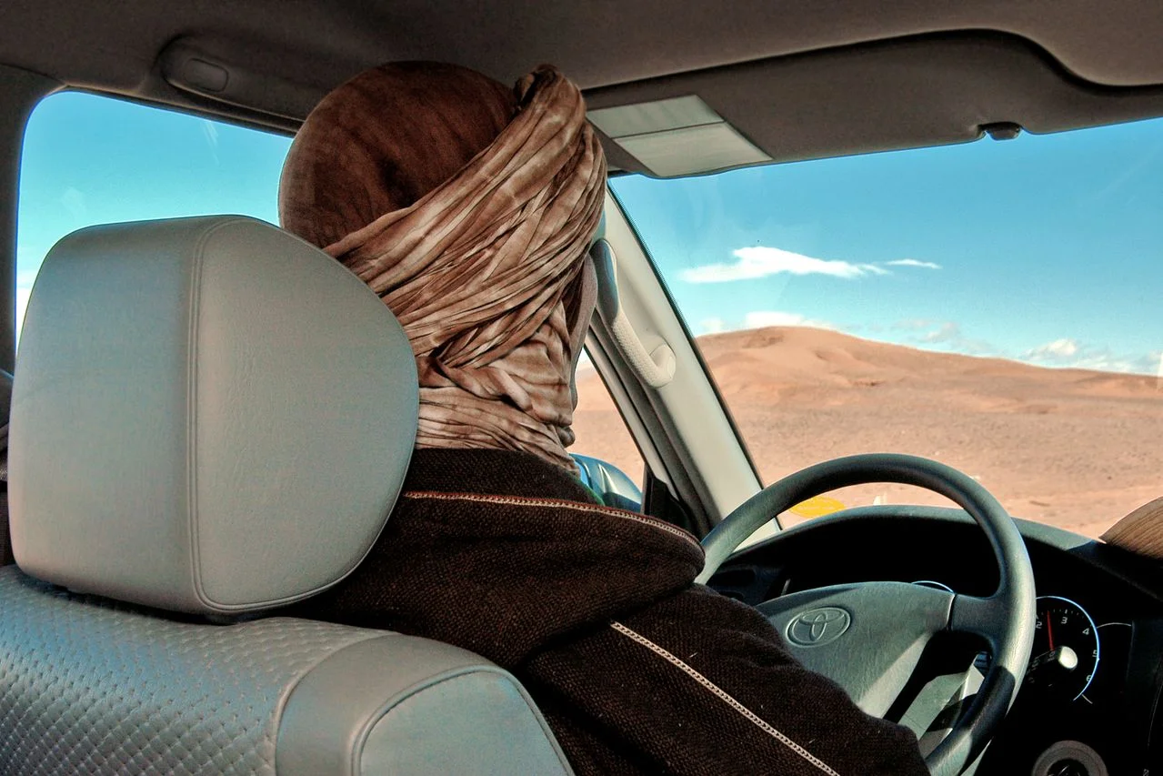 Driver in a traditional headscarf at the wheel of a 4x4 heading into the desert